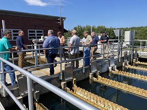 During a CPE event in South Carolina several  state, federal and system staff stand together on the walkway between the settling basins and conventional filters collecting information by speaking with an operator from the facility