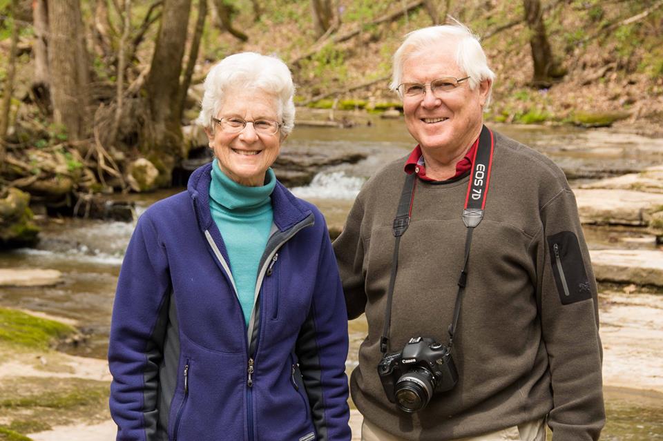 Man and woman standing together in front of a wooded creek