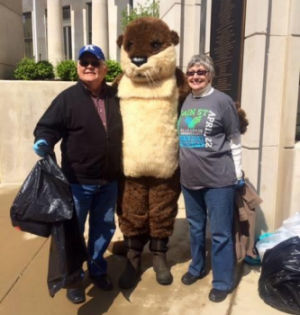 Mascot Ollie the Otter stands with two other people at an outreach event.